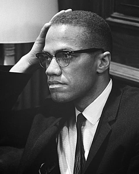 Malcolm X en 1964, con lentes, apoyando la cabeza en la mano.